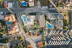Top down aerial view of hotels roofs, streets with parked cars and swimming pools with blue water in resort city near the sea