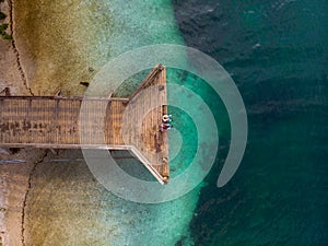 Top down aerial view. A loving couple are sitting on a wooden bridge, a pier. Sunny day, clear water, mountain lake. The concept