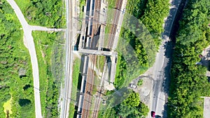 Top down aerial view of railway and train station surrounded by parks and fields with green grass and autumn color trees on a sunn