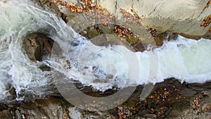 Top down aerial view of small mountain stream with fast moving clear water between rocky stones in autumn.