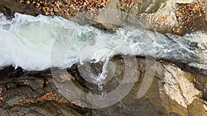 Top down aerial view of small mountain stream with fast moving clear water between rocky stones in autumn.