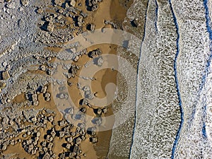 Top down aerial view of waves breaking onto a sandy beach with large boulders Southerndown
