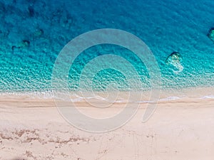 Top-down aerial view of a white sandy beach on the shores of a beautiful turquoise sea.