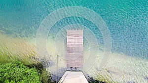 A top down aerial view of a wooden pier on a forest lake on a sunny day. The camera tilted down, dolly in over the