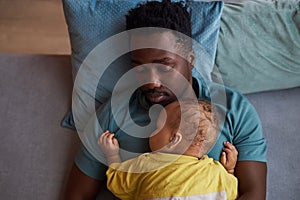 Top down Black father with baby son sleeping together at naptime