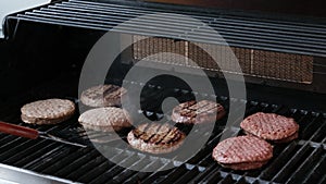 The top down, close up view of several hamburgers cooking on the grill. Someone is flipping the burgers and the flames