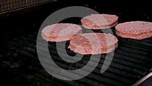 The top down, close up view of several hamburgers cooking on the grill. Someone is flipping the burgers and the flames