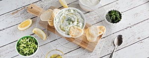 A top down cropped view of a bowl of tzatziki dip with pita bites ready for snacking.