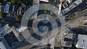 Top down descending footage of road intersection in city. Vehicles driving in streets and standing in car park.