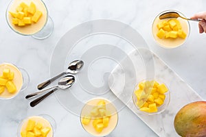Top down of dessert dishes of mango mousse with a hand taking a spoonful out of one.