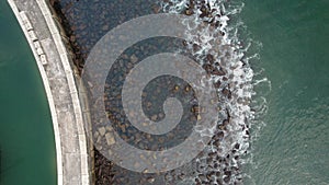 Top down drone shot of ocean waves crashing against a seawall coastal defence with birds flying away, captured in Portugal