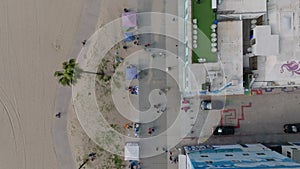 Top down panning footage of people strolling on pavement along Venice sand beach with stands and shops. Los Angeles