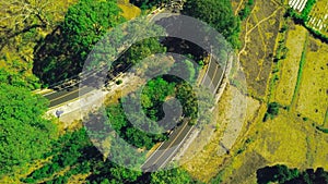 Top down shot at curvy road in the countryside with vehicles making turns.