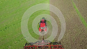 Top down shot of red tractor working on green field plowing soil