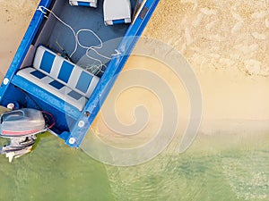 Top down view from above on blue metal fishing boat with engine moored on sandy beach of lake or river with clear water. Motorboat