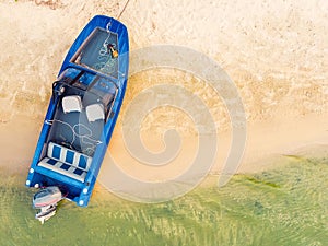 Top down view from above on blue metal fishing boat with engine moored on sandy beach of lake or river with clear water. Motorboat