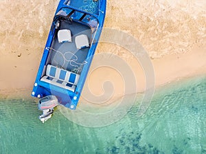 Top down view from above on blue metal fishing boat with engine moored on sandy beach of lake or river with clear water. Motorboat