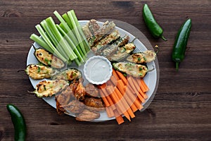 Top down view of an appetizer plate of wings, jalapeno poppers and zucchini sticks served with carrot and celery sticks.