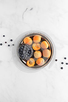 A top down view of apricots and a small bowl of blueberries on a metal tray. A complimentary colour concept.