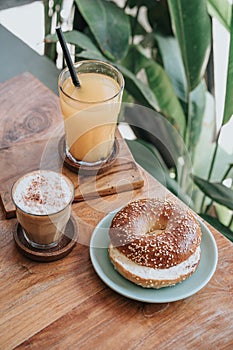 Top-down view of a bagel, and two glass drinks on plate and on a wooden table