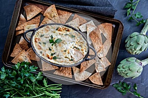 Top down view of a baking sheet filled with pita triangles and a hot artichoke dip in the middle.