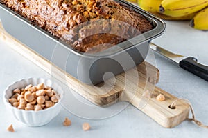 Top down view of a banana bread loaf fresh out of the oven with a small bowl of butterscotch chips.