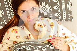 Top down view, blurred young woman laying in bed in her pyjama, holding thermometer in focus. Grip / flu sickness concept