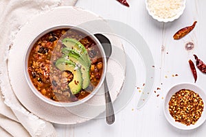 Top down view of a bowl of chili topped with avocado slices and chili flakes.