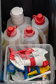 Top down view of a bucket with various colorful cleaning supplies and spray bottle tops and pumps