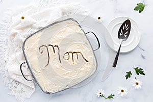 Top down view of a cake with the word Mom carved in the cream cheese frosting, ready for serving. A Mother's Day concept