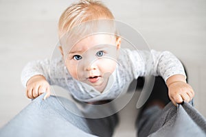 Top down view of cheerful baby boy infant taking first steps holding to father& x27;s sweatpants at home. Cute baby boy