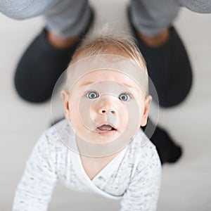 Top down view of cheerful baby boy infant taking first steps holding to father& x27;s sweatpants at home. Cute baby boy