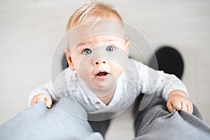 Top down view of cheerful baby boy infant taking first steps holding to father& x27;s sweatpants at home. Cute baby boy