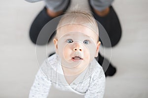 Top down view of cheerful baby boy infant taking first steps holding to father& x27;s sweatpants at home. Cute baby boy