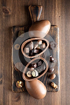 Top down view of chocolate Easter egg halves filled with gourmet chocolates, on a wooden board.
