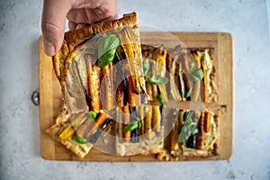 Top down view of a colorful rainbow carrot pie with ricotta and basil one piece grabbed by a male hand close-up, horizontal