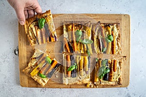 Top down view of a colorful rainbow carrot pie with ricotta and basil one piece grabbed by a male hand, horizontal