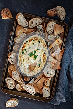 Top down view of a cookie sheet filled with various pieces of bread and pita triangles with artichoke dip in the middle.