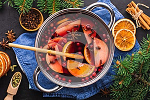 Top-down view of a cooking pot of hot wine with aromatic spices on a black textured background.