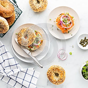 Top down view of everything bagels topped with cream cheese, smoked salmon lox and garnished with capers and sprouts.