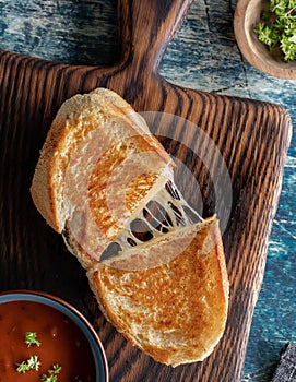 Top down view of a homemade grilled cheese sandwich on a wooden board, served with tomato soup.