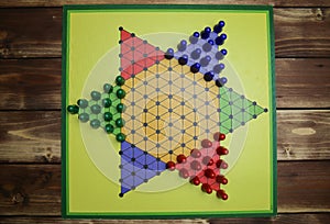 Top down view on isolated yellow gamboard with hexagon, multicolored game pieces, wooden background - chinese checkers sternhalma