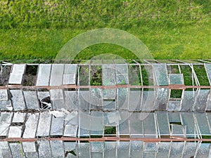 Top down view of a large, abandoned green house showing multiple broken glass roof structures.
