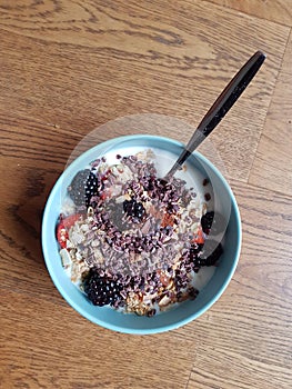Top down view of light blue healthy breakfast bowl with granola, yoghurt and fruits on wooden floor background