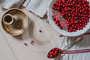 Top down view on lingonberries in a bowl and on a spoon, linen tablecloth and candlestick on wooden table in bright sunlight,