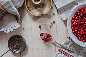 Top down view on lingonberries in a bowl and on a spoon, linen tablecloth, incense and candlestick on wooden table in bright