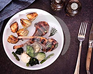 Top down view of a plated grilled lamb chops meal with potatoes and vegetables.