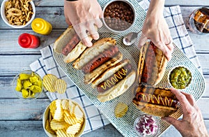 A top down view of a platter of gourmet hotdogs with hands helping themselves to a hotdog.