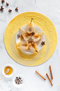 Top down view of poached and torched pears along with cinnamon sticks, star anise, a bowl of cloves and honey.