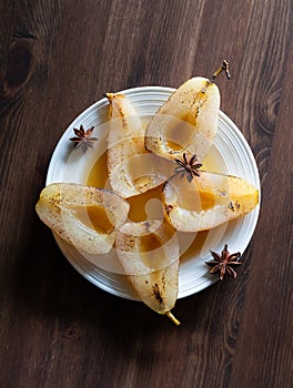 Top down view of a poached and torched pears with star anise on a dark wooden table.